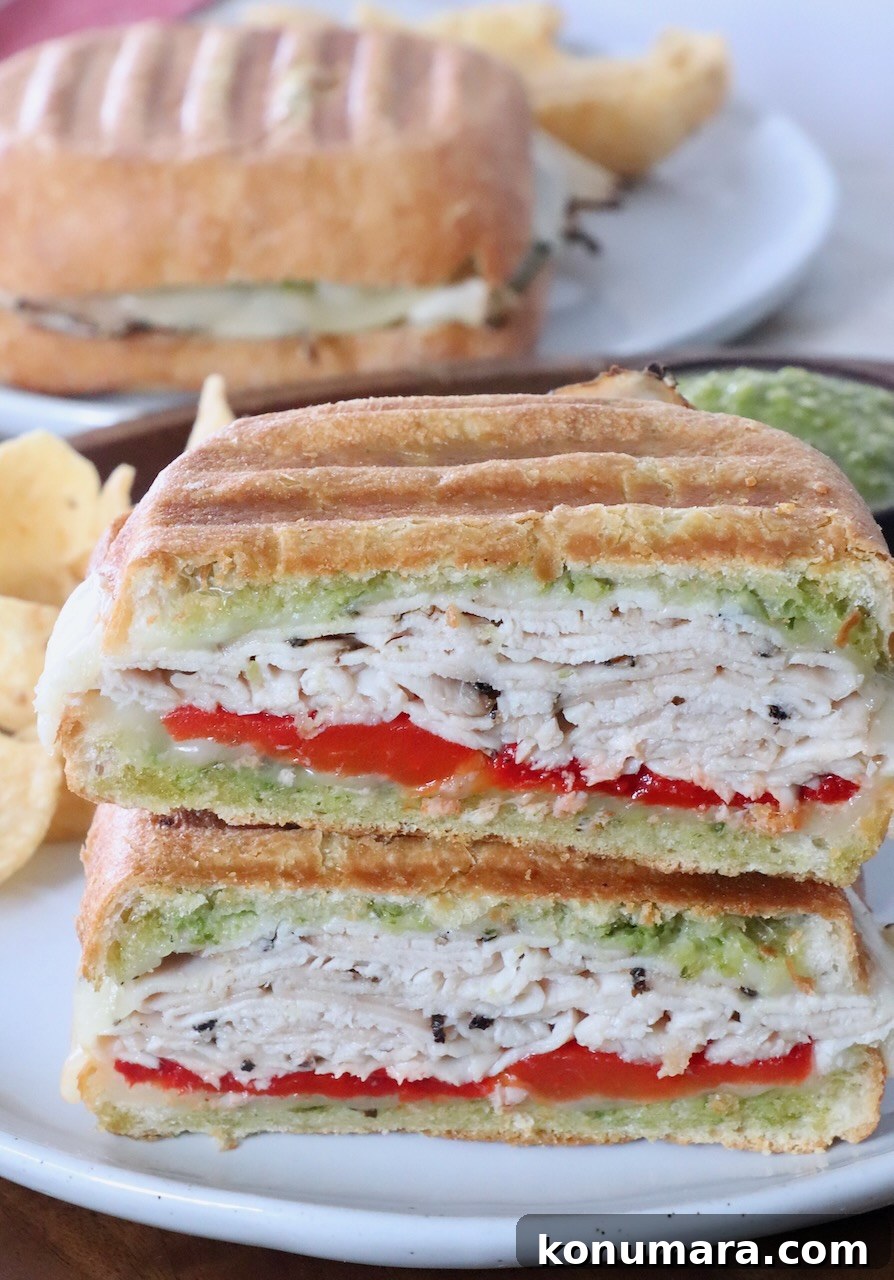 Grilled Turkey Pesto Sandwich with Melted Mozzarella 2 turkey sandwich sliced in half on stacked up on plate