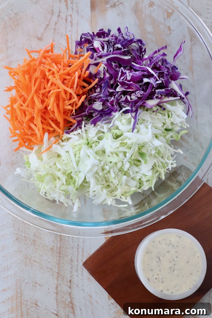 Classic Creamy Coleslaw Recipe 3 shredded cabbage and carrots in large glass bowl next to a small bowl of coleslaw dressing