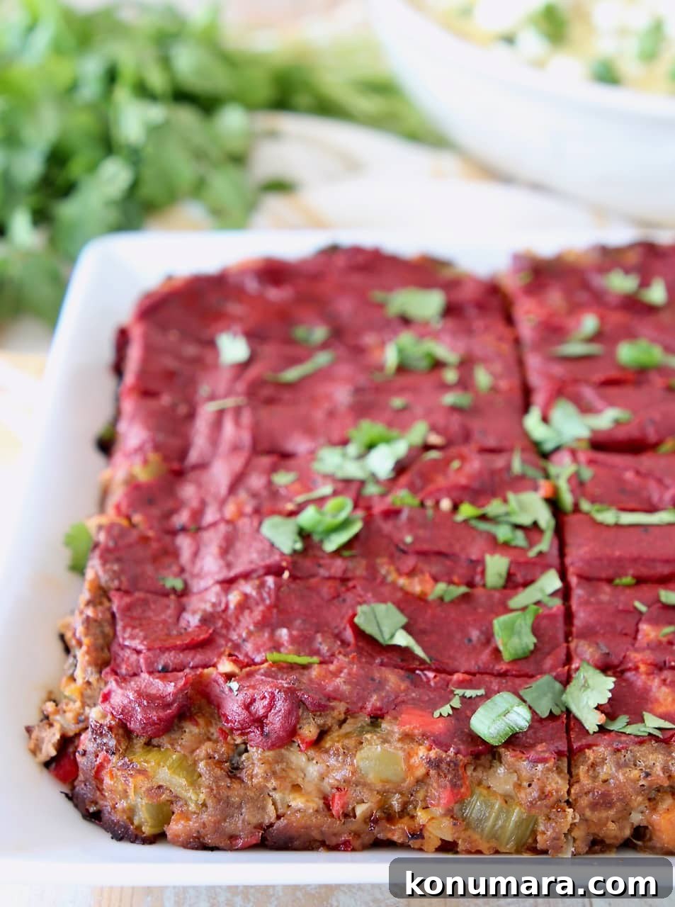 Mexican meatloaf topped with tomato paste, sliced on a white plate with fresh cilantro