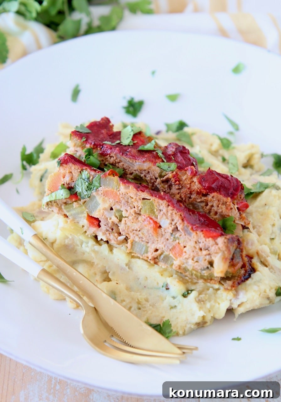 Two slices of Mexican meatloaf on top of mashed potatoes on plate with a gold fork and knife