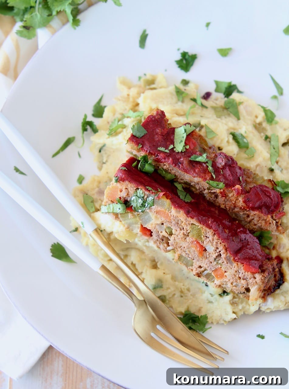 Two slices of Mexican meatloaf on top of mashed potatoes on white plate with fresh cilantro