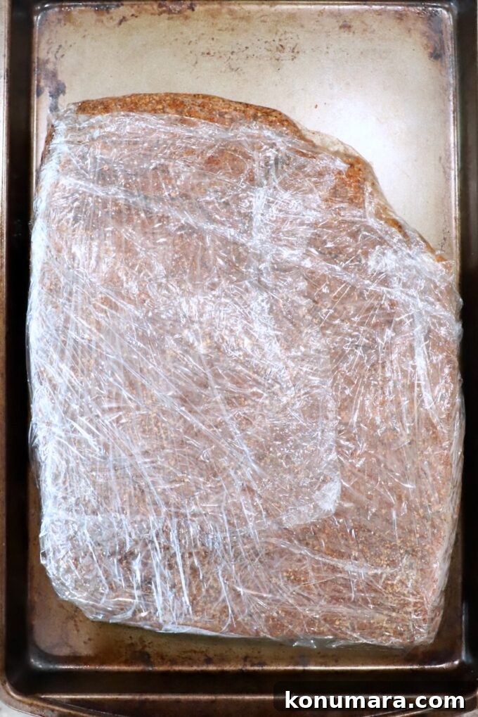 seasoned brisket wrapped in plastic wrap on baking sheet