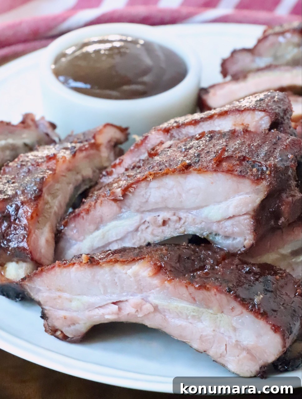 sliced smoked baby back ribs on a plate with a small bowl of bbq sauce