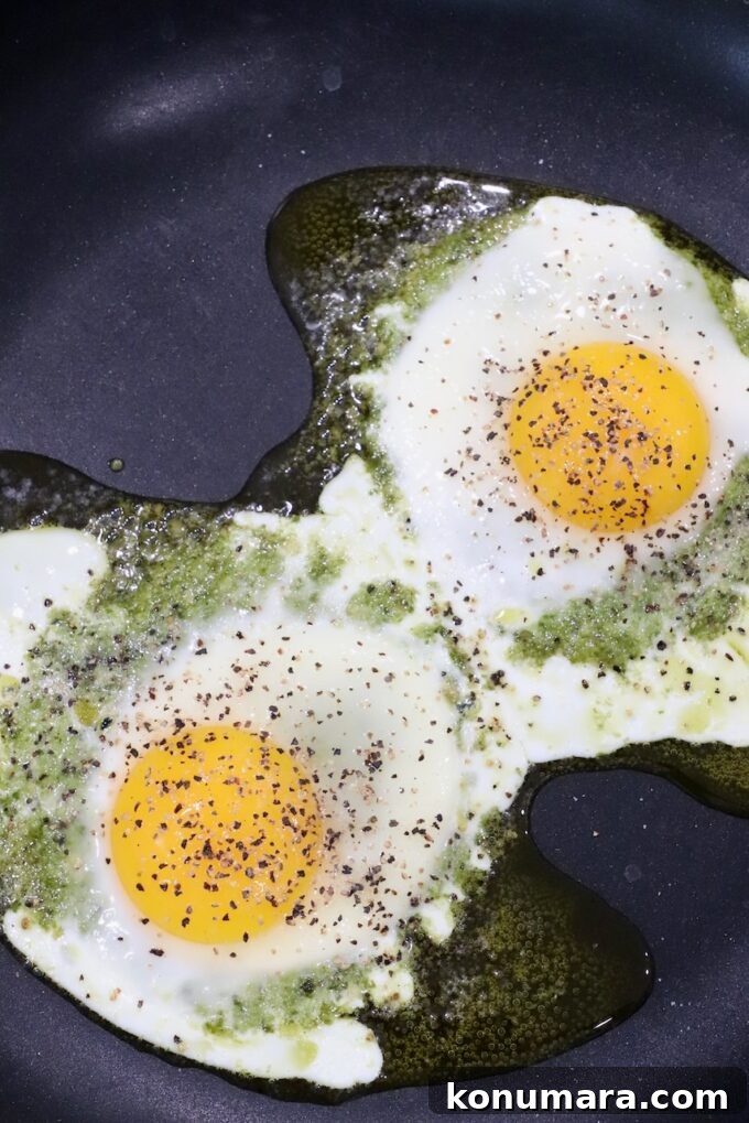 Creamy Pesto Scrambled Eggs with Parmesan 8 cooked eggs on top of pesto in skillet, seasoned with salt and pepper