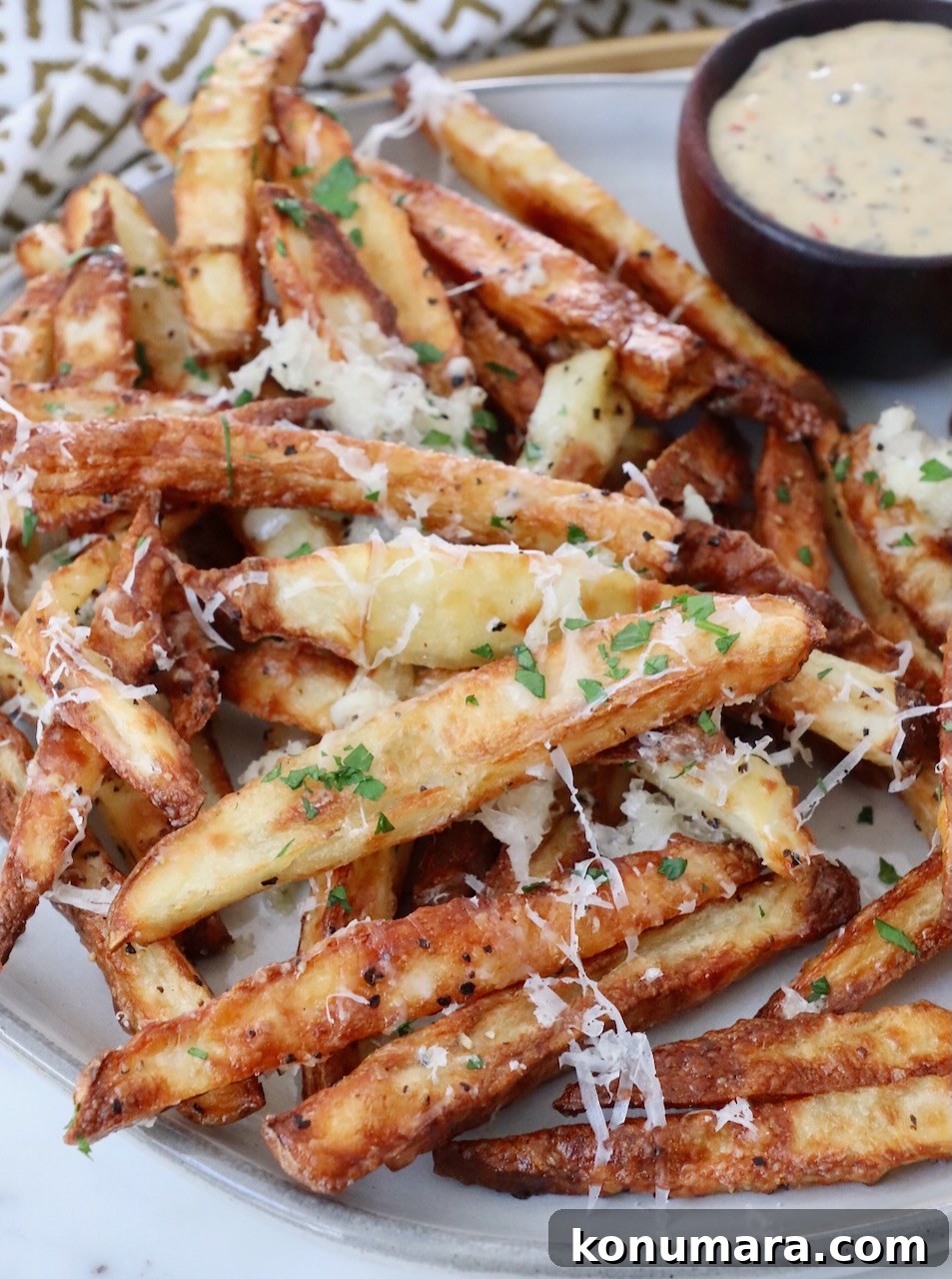 Crispy Truffle Fries with Garlic and Parmesan 2 parmesan truffle fries on plate with a small bowl of dipping sauce on the side