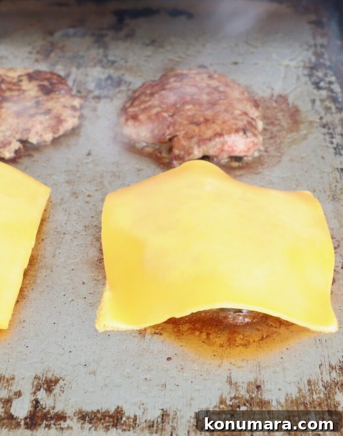 sliced of cheese on top of cooked burger patties on flat top