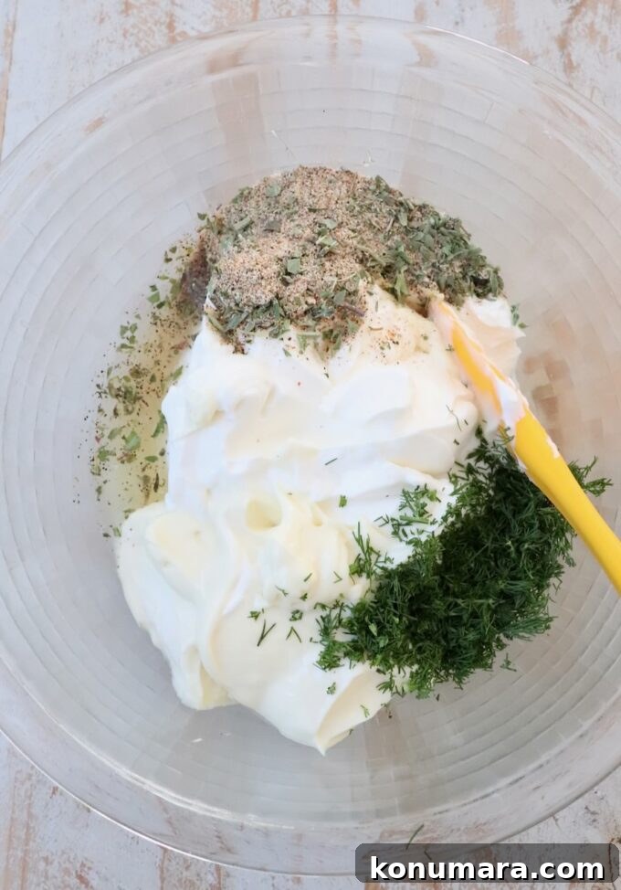 ingredients for vegetable dip in large glass bowl with yellow spatula