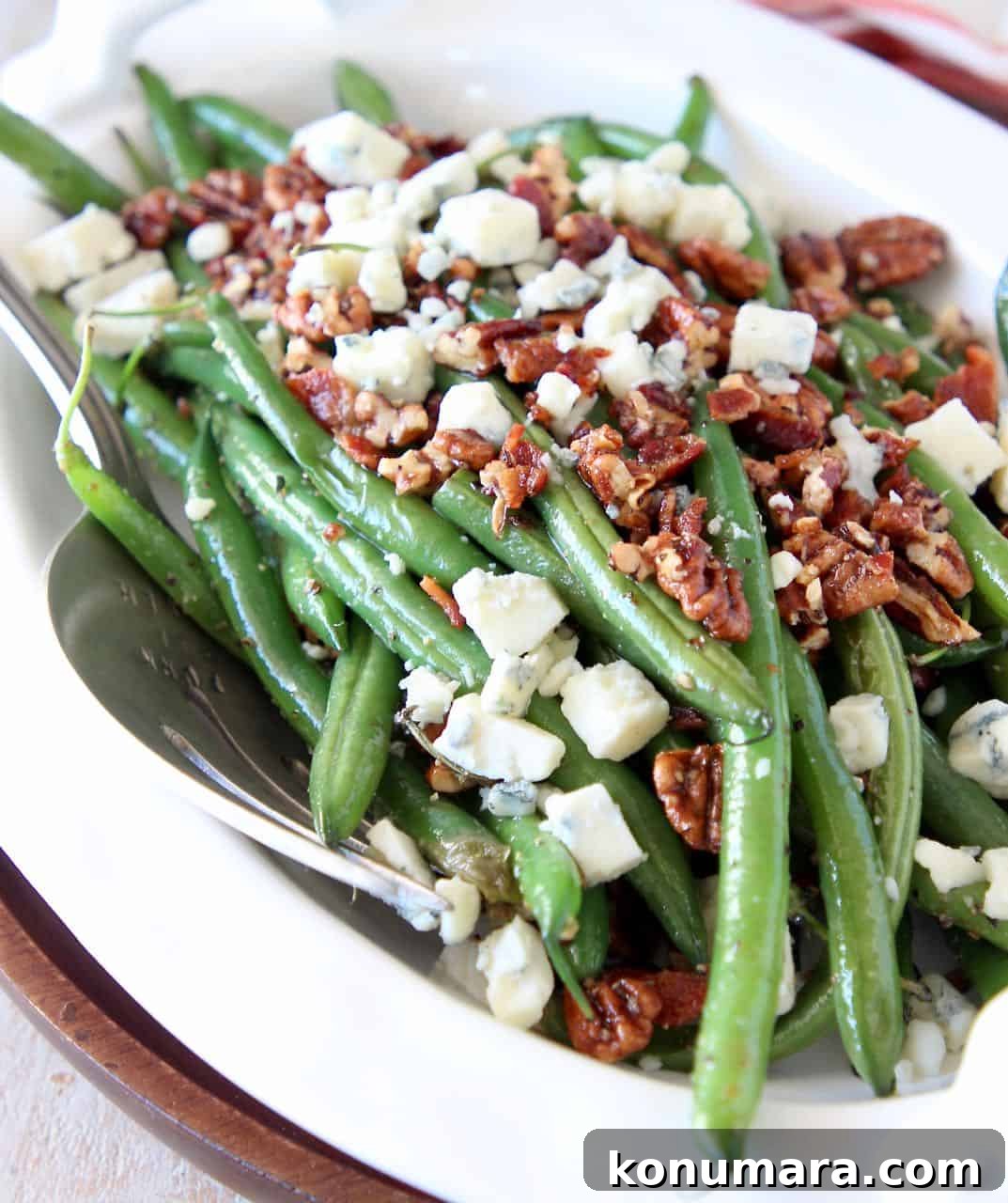 Fresh cooked green beans in serving bowl topped with crumbled bacon, pecans and blue cheese