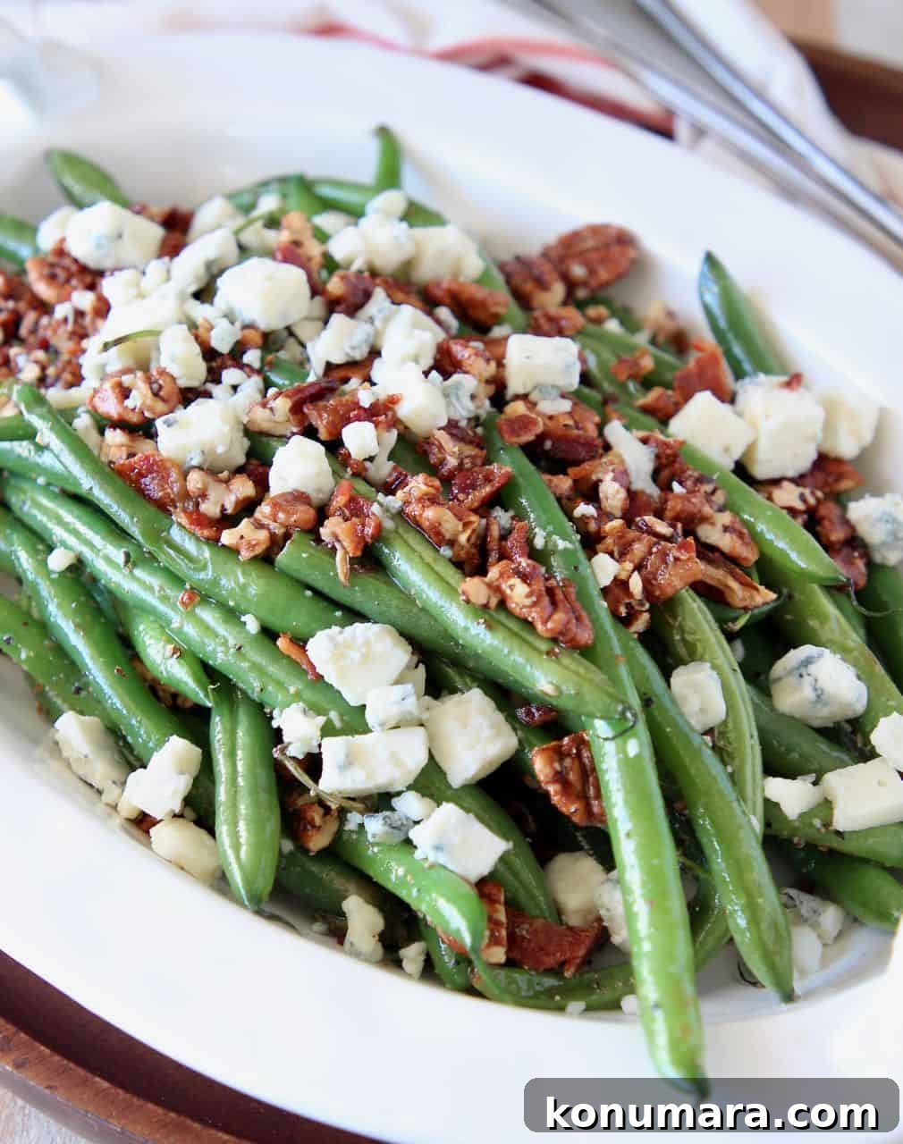 Fresh green beans in serving bowl, topped with pecans and blue cheese crumbles