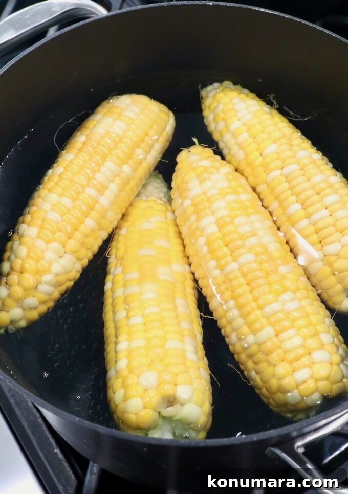 Corn cobs in boiling water in pot on the stove