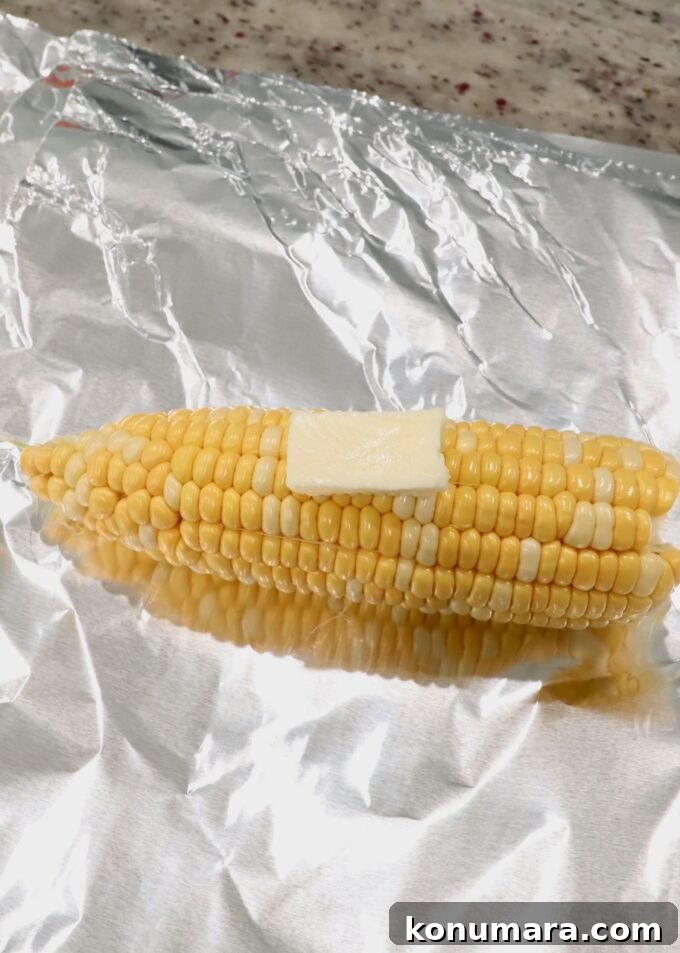 Corn on the cob with the husks removed on piece of foil with slice of butter on top