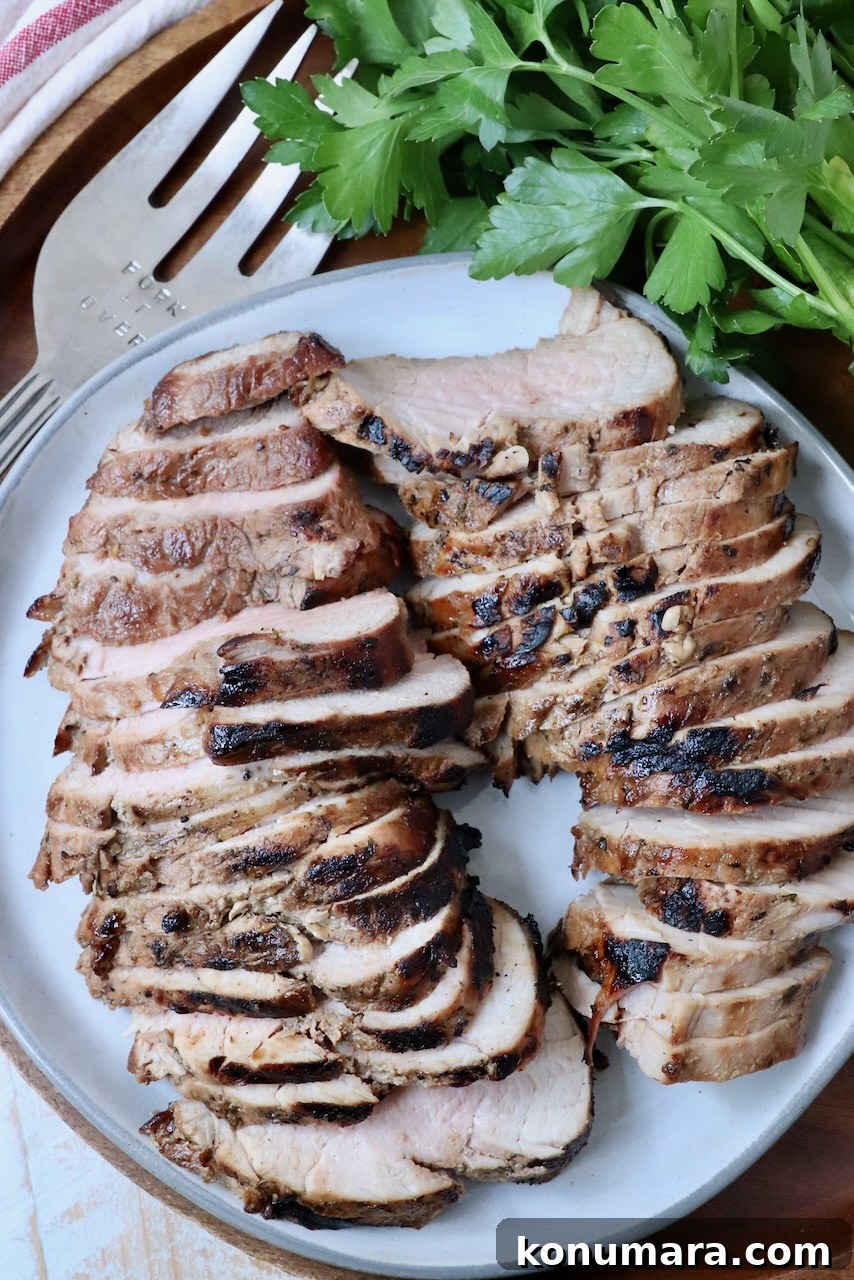 Savory Pork Tenderloin Marinade for Tender, Juicy Meat 2 sliced pork tenderloin on plate with serving fork and fresh parsley on the side
