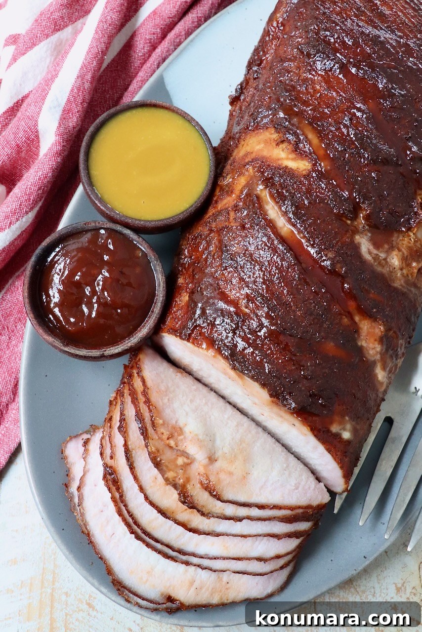 partially sliced smoked pork loin on plate with two sides of bbq sauce