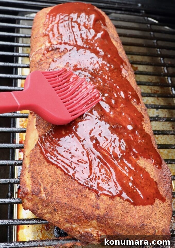 How to Smoke Pork Loin for Tender, Juicy Results 7 pork loin on smoker being brushed with bbq sauce