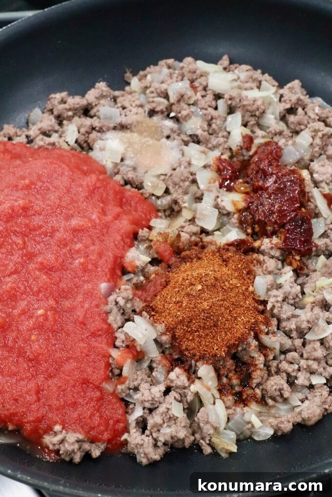 seasoned ground beef with a can of crushed tomatoes in a skillet