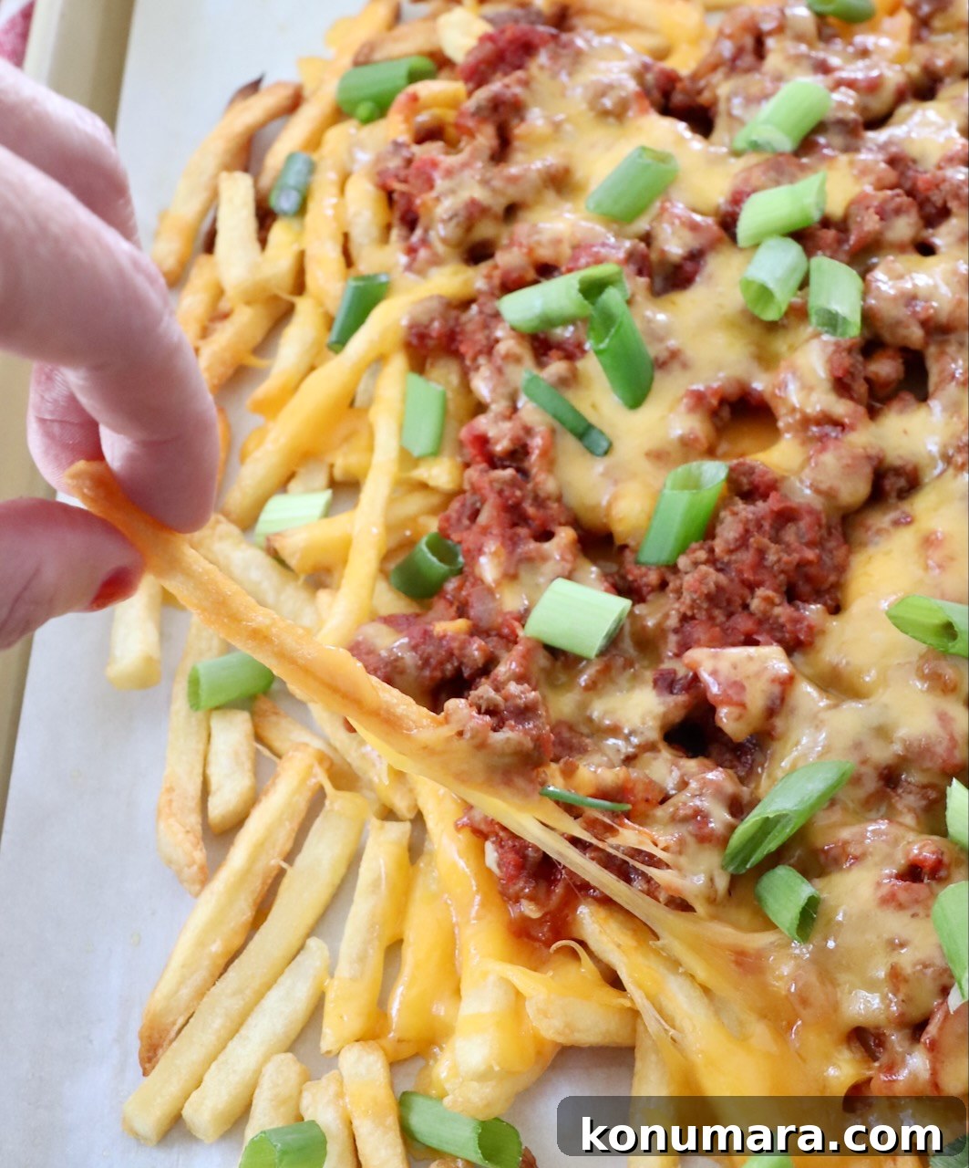 hand pulling cheese fry from baking sheet of chili cheese fries