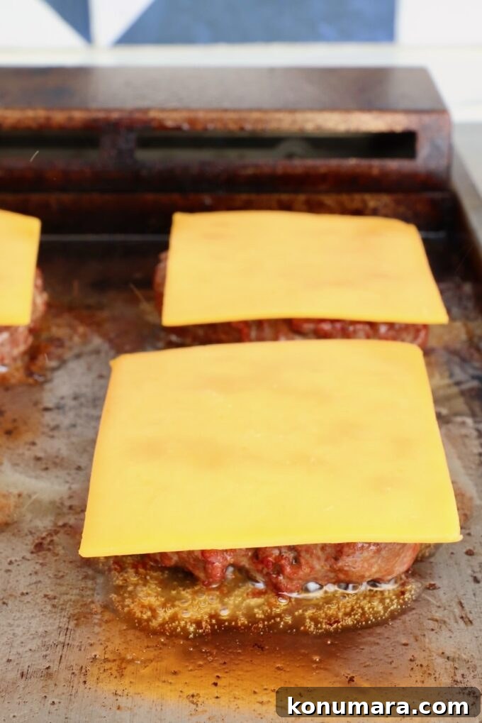 smoked burger patties on a flat top griddle topped with slices of cheese