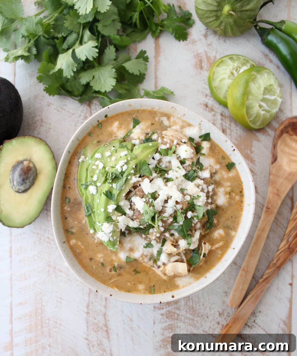 Creamy Green Chili Chicken Enchilada Soup Recipe 2 Green Chili Chicken Enchilada Soup topped with avocado, cilantro, and cheese on a wooden surface.