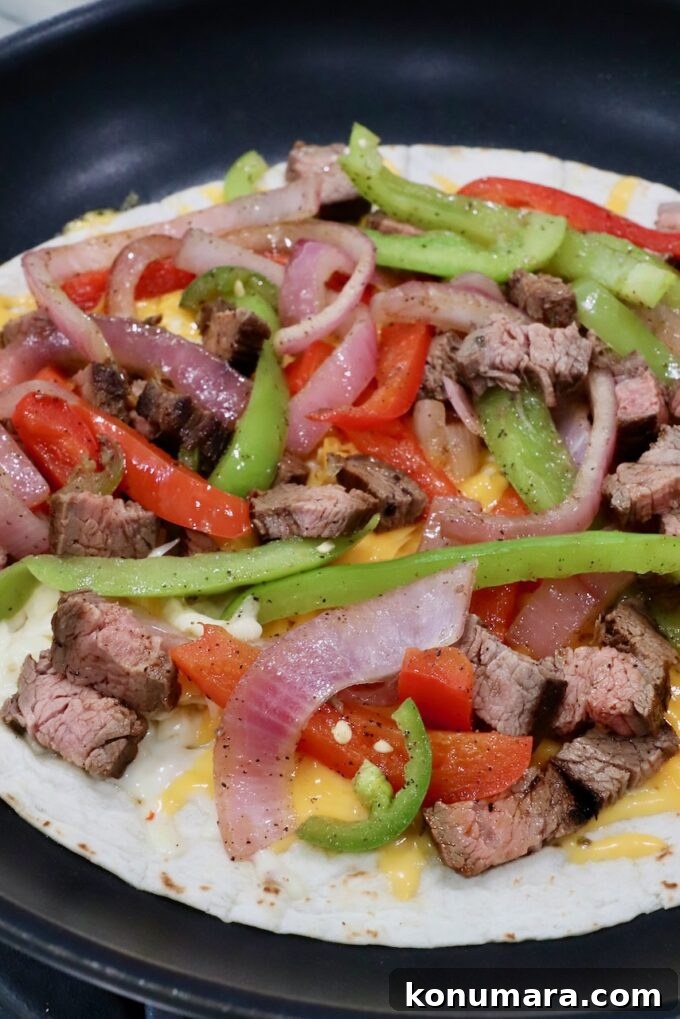 Steak Quesadillas Recipe with Melted Cheese and Salsa 7 fajita veggies and grilled steak on top of shredded cheese on tortilla in skillet