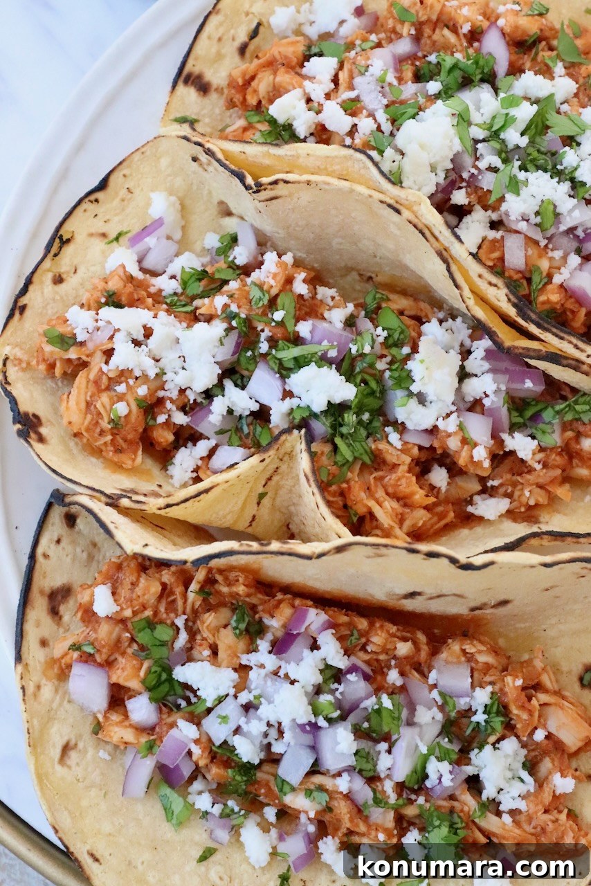Smoky Chipotle Chicken Tinga Recipe 2 chicken tinga tacos on plate topped with diced onions and cilantro