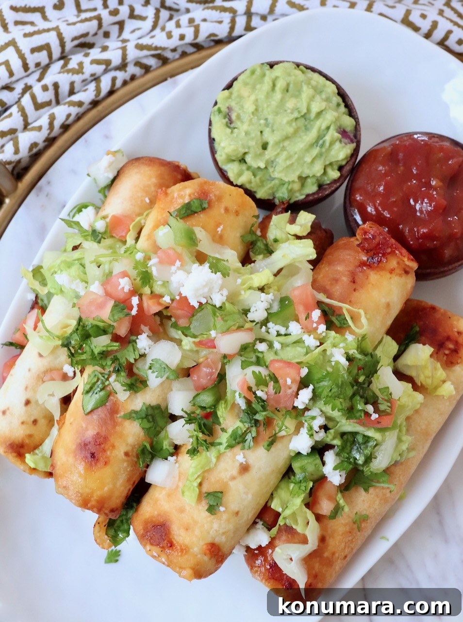 Homemade Crispy Beef Taquitos Recipe 10 taquitos stacked up on plate topped with guacamole and pico de gallo