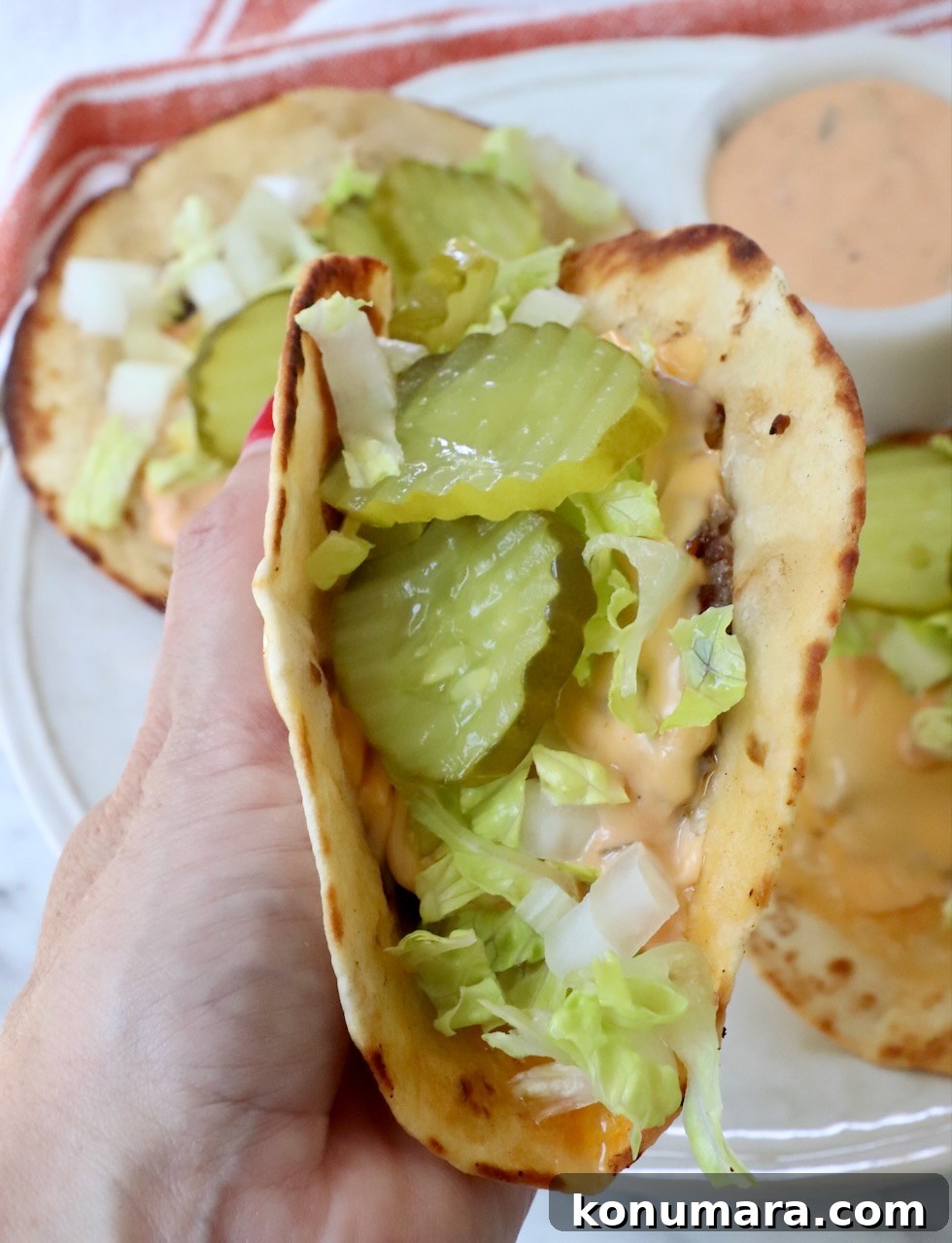 Smash Burger Taco Recipe: Crispy Smashed Patties 11 Hand holding smash burger taco filled with pickles and lettuce