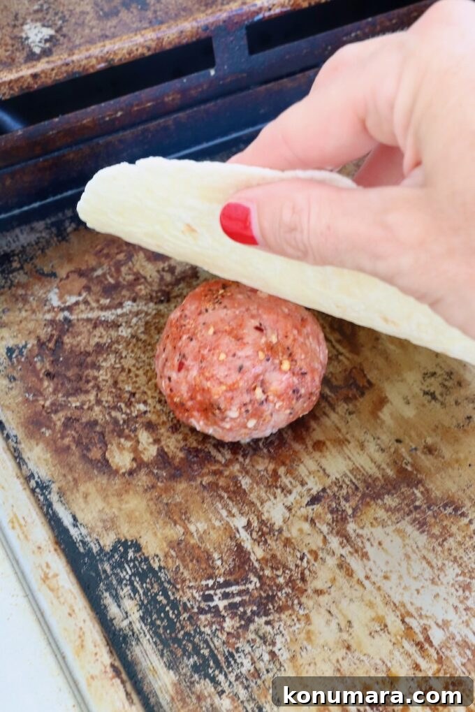 Smash Burger Taco Recipe: Crispy Smashed Patties 4 Ball of beef on a griddle with a hand holding a tortilla above it