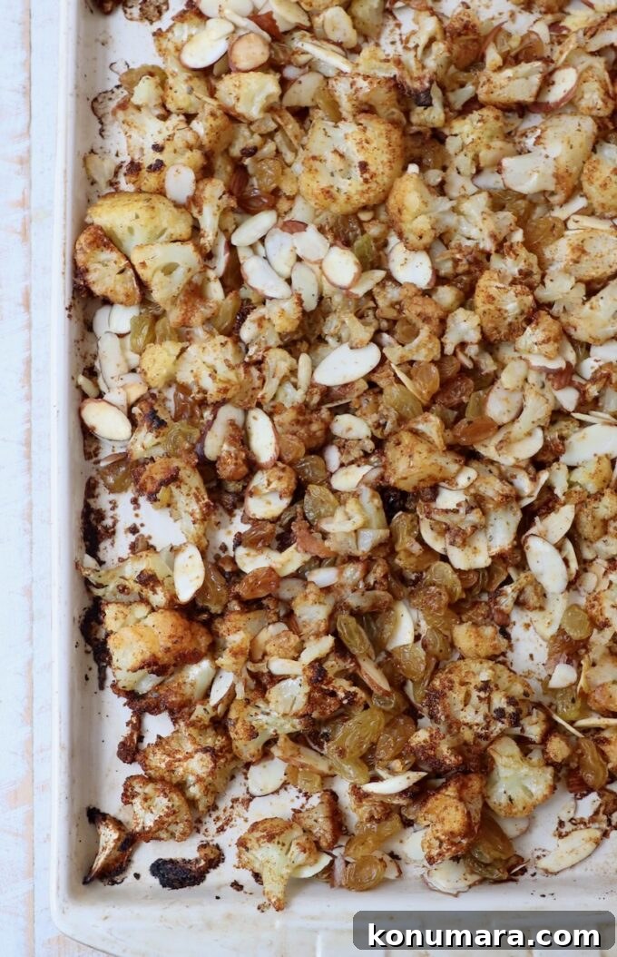 roasted seasoned cauliflower on baking sheet with almonds and raisins