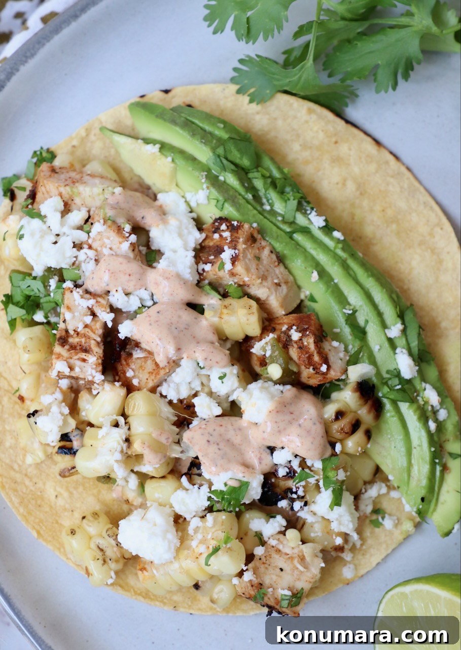 Elote Chicken Tacos with Mexican Street Corn 2 taco on plate topped with avocado and chili lime sauce