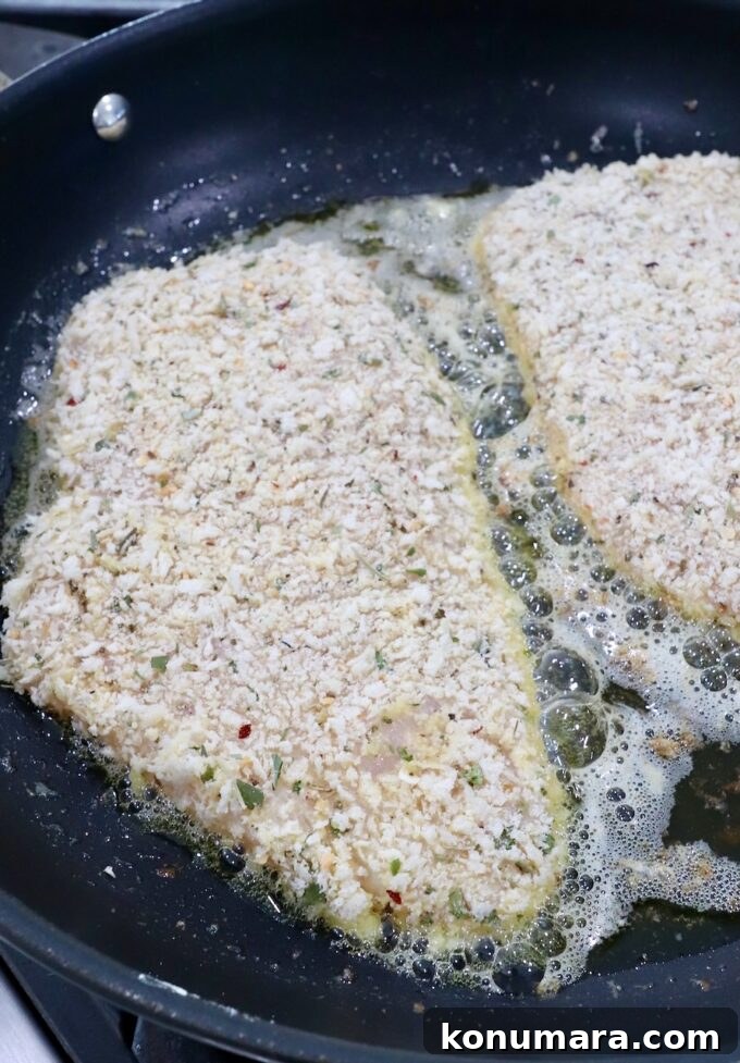 Crispy Parmesan-Crusted Chicken Recipe 11 breadcrumb coated chicken breasts cooking in oil in a skillet