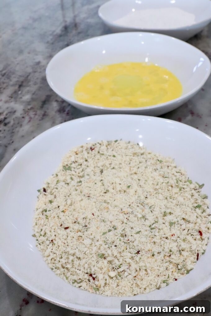 Crispy Parmesan-Crusted Chicken Recipe 5 three bowls filled with seasoned breadcrumbs, whisked eggs and flour