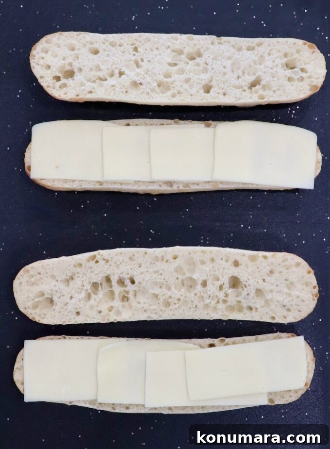 Classic Meatball Sub Recipe with Marinara and Mozzarella 5 two demi baguettes sliced in half on cutting board, topped with sliced mozzarella cheese