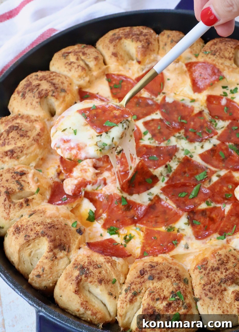 pizza dip in a cast iron skillet with pull apart bread around the outside and spoon scooping out the dip