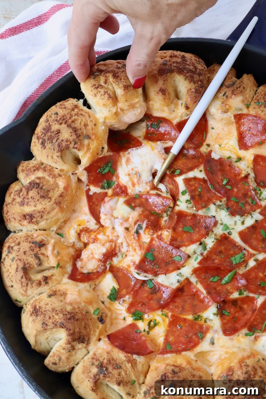 hand pulling piece of bread from a skillet with pizza dip