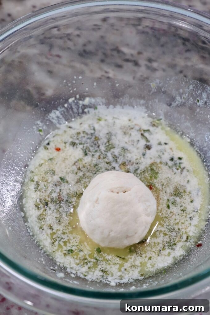 ball of biscuit dough rolled in melted butter with herbs in a glass bowl
