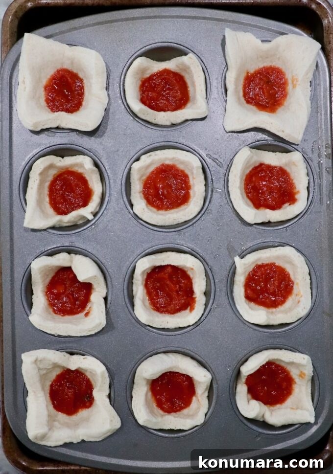 pizza dough squares pressed into a muffin tin and filled with marinara sauce