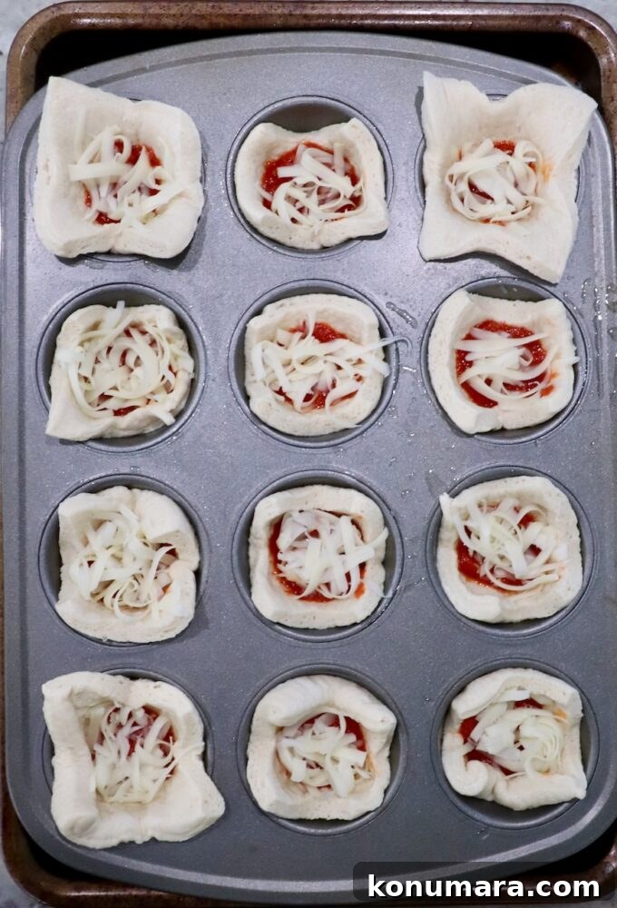 pizza dough squares pressed into a muffin tin and filled with marinara sauce and cheese