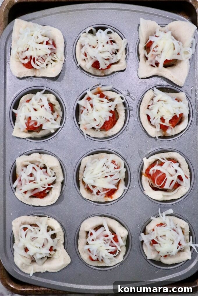 pizza dough squares pressed into a muffin tin and filled with marinara sauce, meatballs and cheese