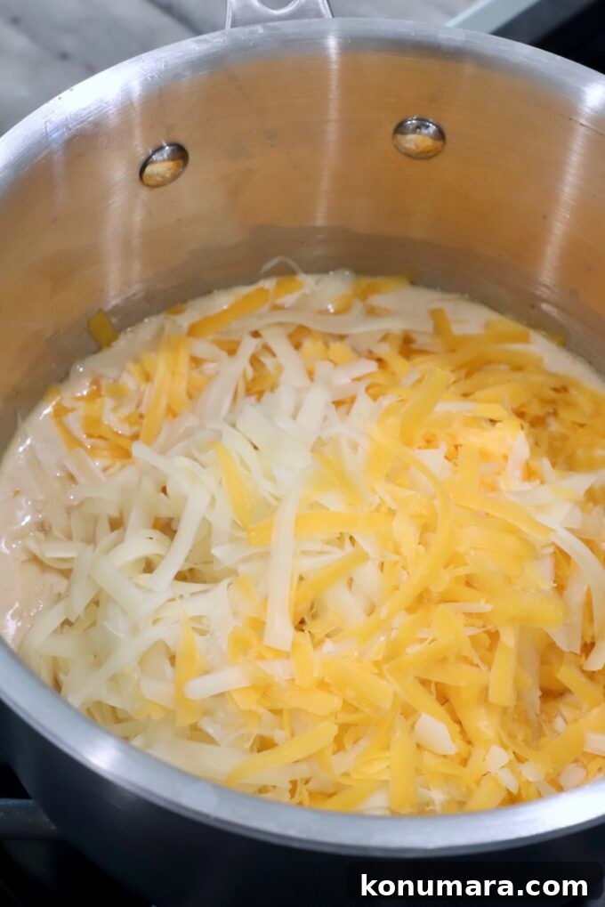 shredded cheese added to a creamy sauce in a pot on the stove
