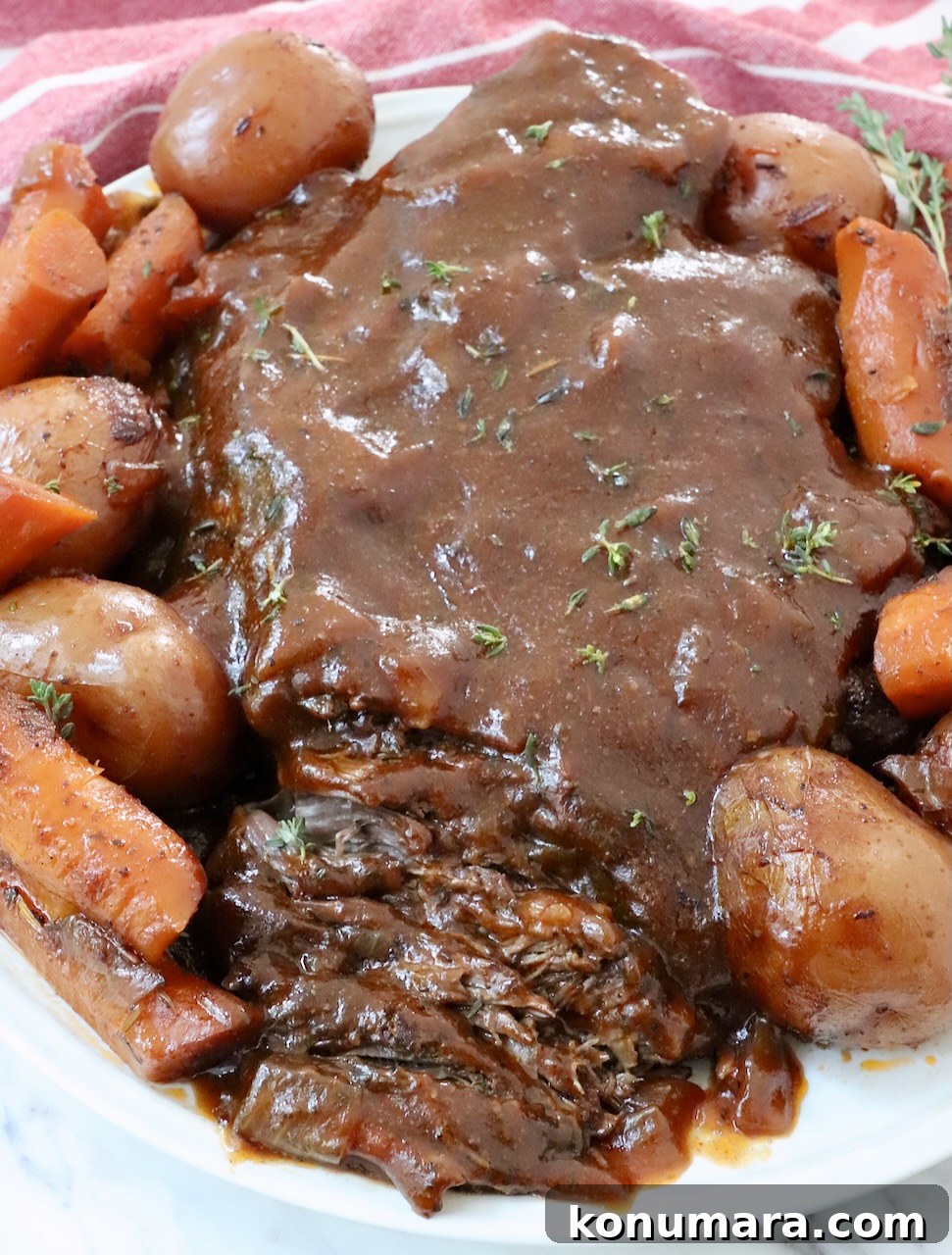 pot roast on plate, topped with gravy, surrounded by roasted potatoes and carrots