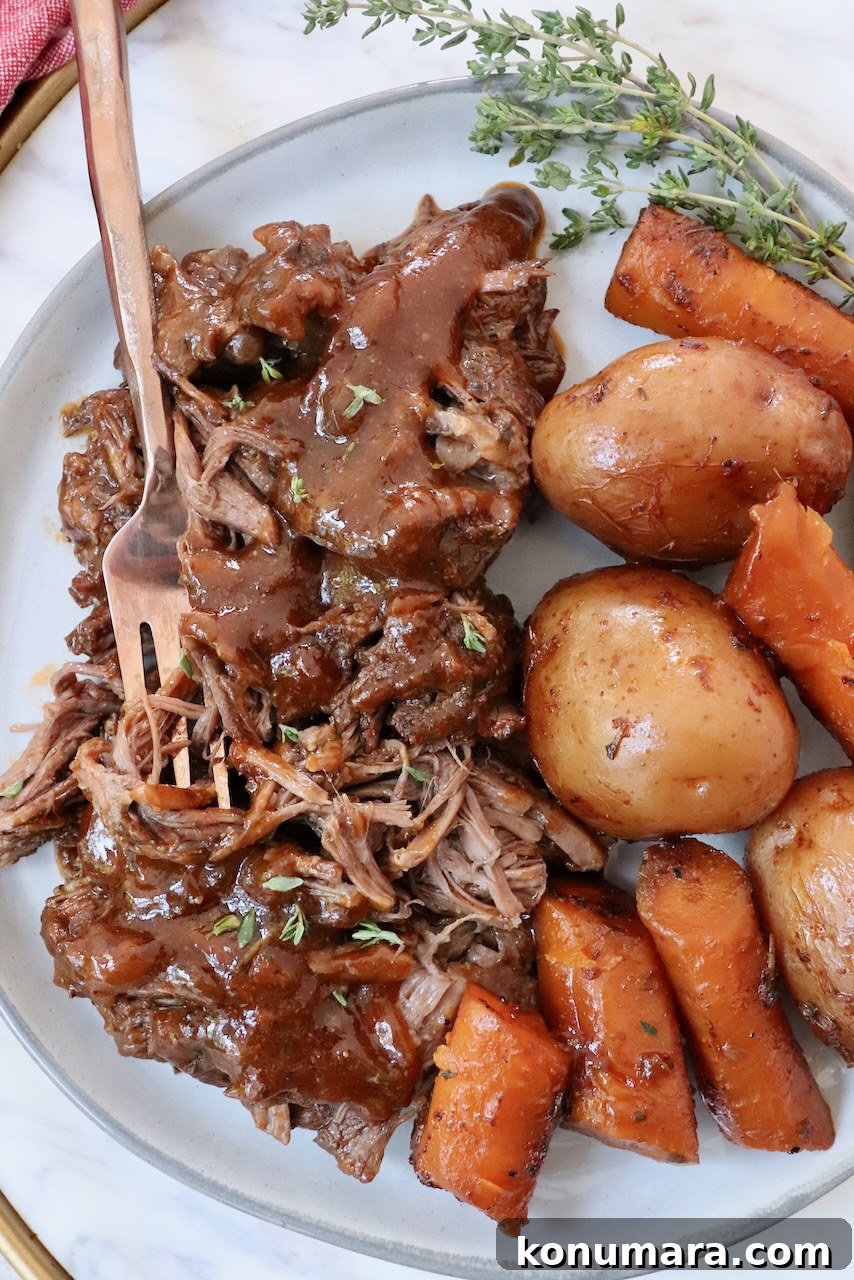 shredded pot roast on plate with gravy, potatoes and carrots