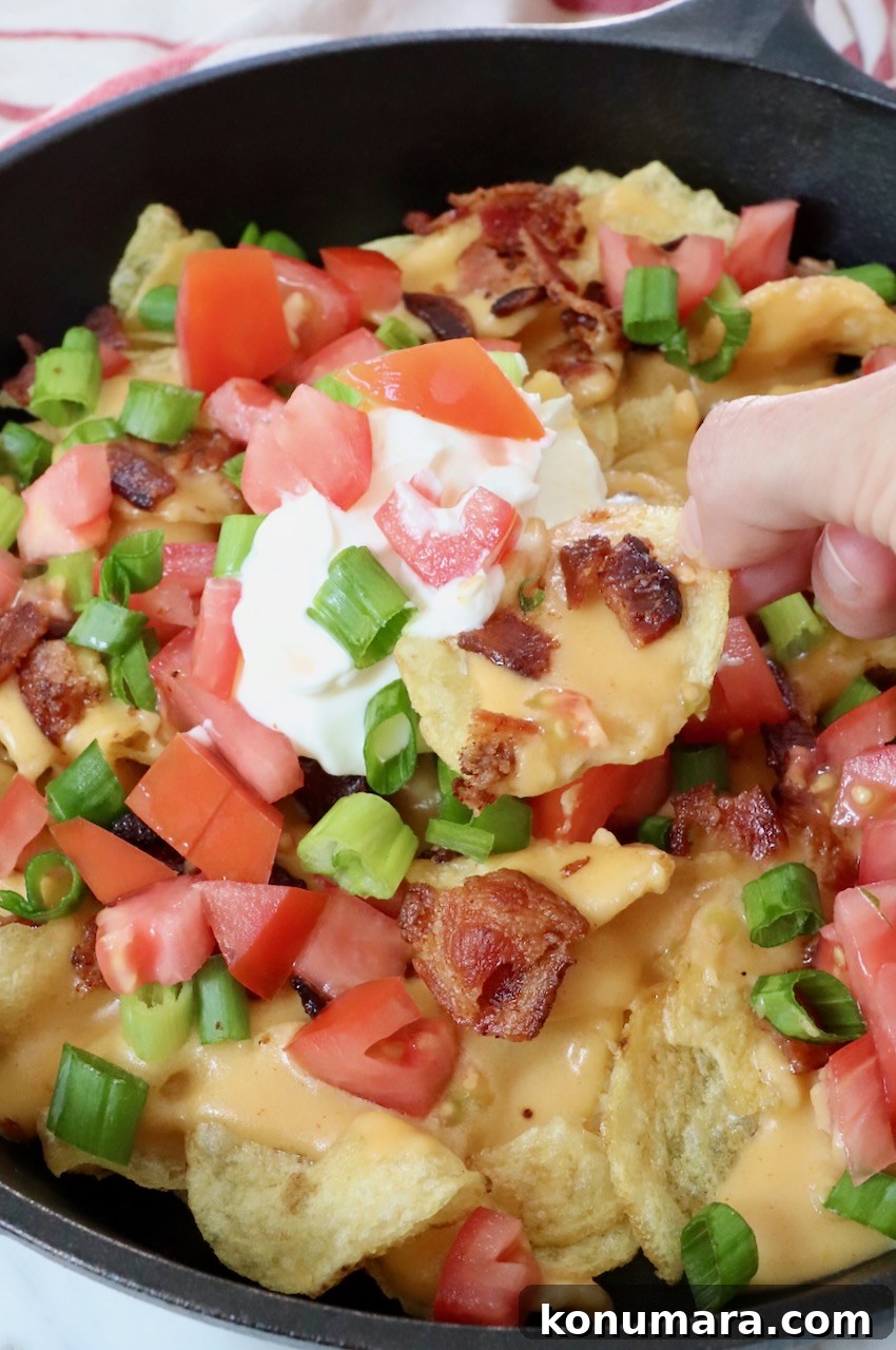 Loaded Irish Nachos with Cheddar, Bacon and Green Onion 2 Irish nachos in a cast iron skillet topped with sour cream