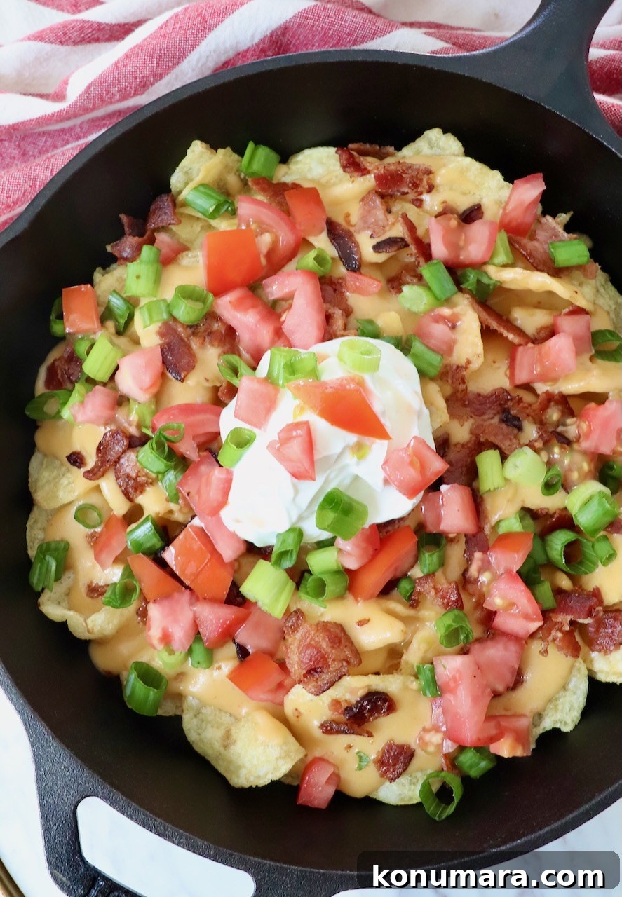 Loaded Irish Nachos with Cheddar, Bacon and Green Onion 6 nachos topped with cheese sauce in a skillet with a dollop of sour cream in the middle