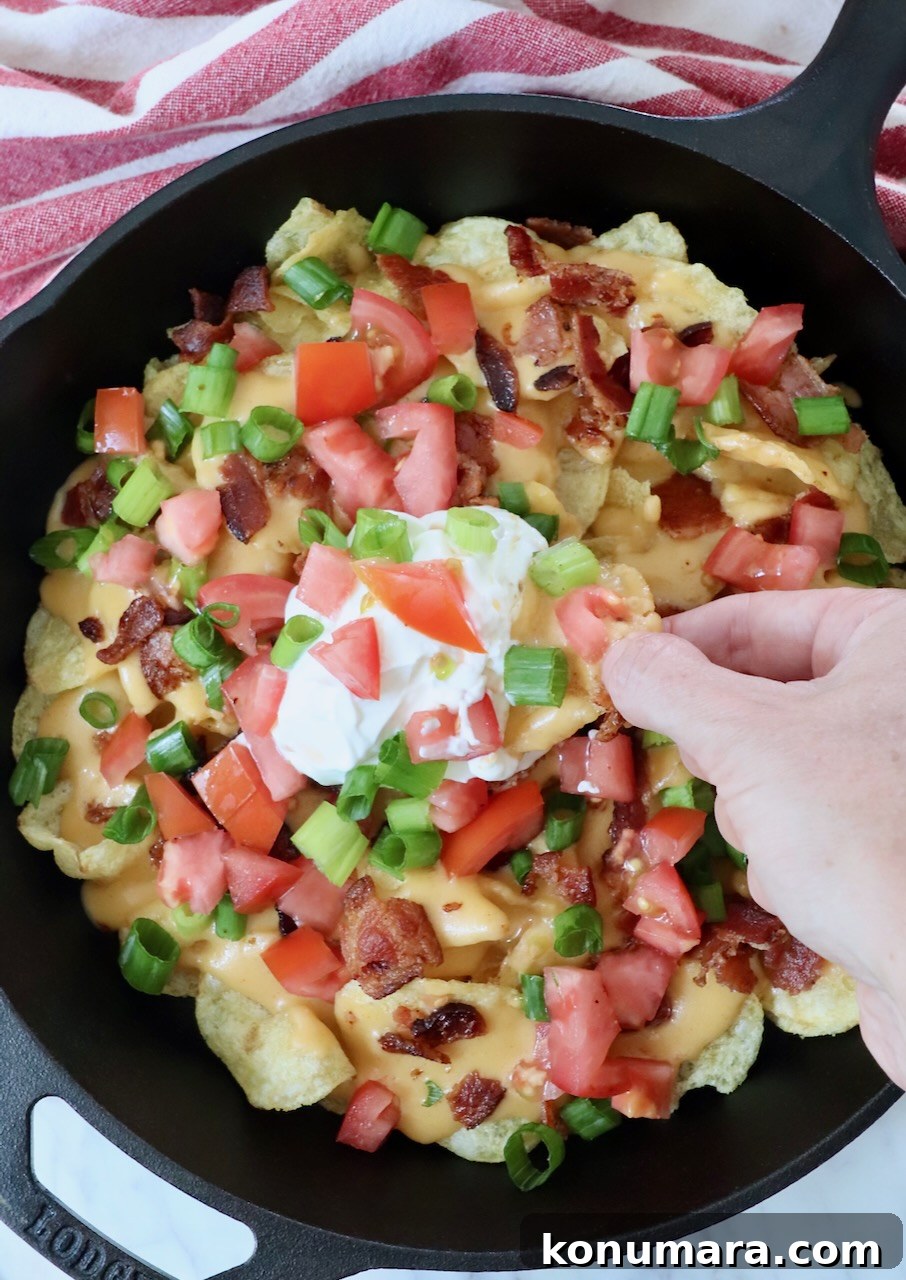 Loaded Irish Nachos with Cheddar, Bacon and Green Onion 7 hand dipping chip into sour cream in a skillet of nachos