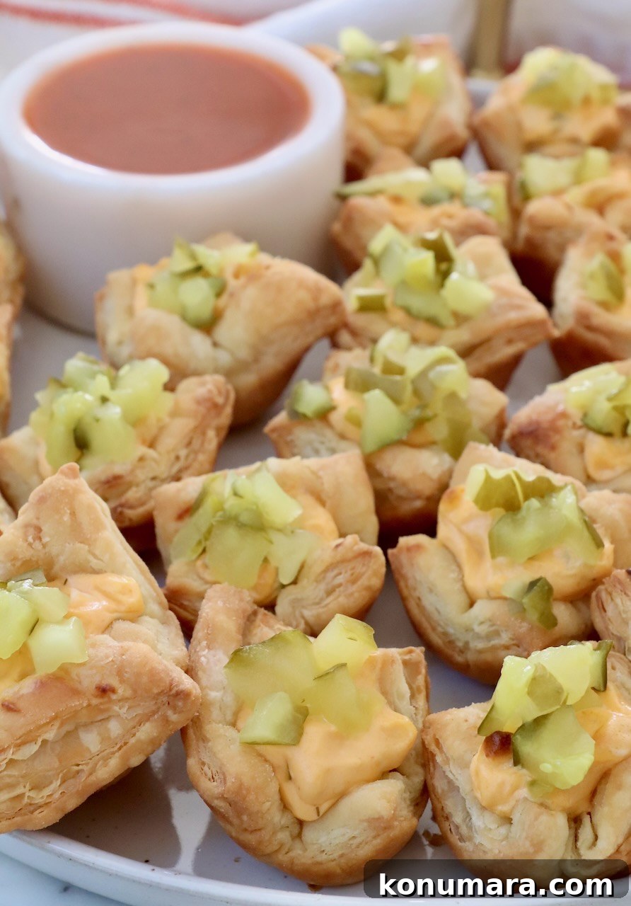 Crispy Puff Pastry Pickle Bites Recipe 2 pickle puff pastry bites on a plate with a small bowl of buffalo sauce