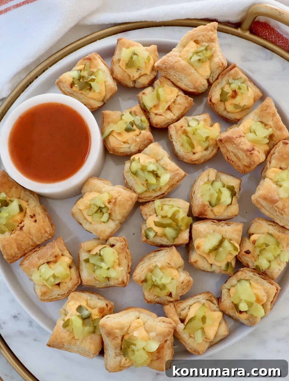 Crispy Puff Pastry Pickle Bites Recipe 6 pickle puff pastry bites on a marble board with a small bowl of hot sauce
