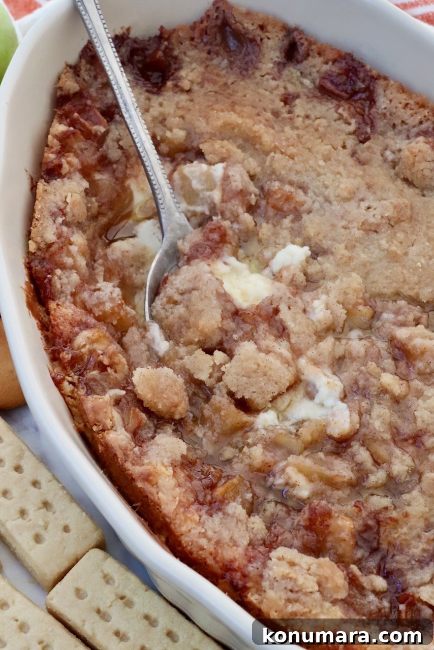 Baked apple pie dip in a casserole dish with a serving spoon