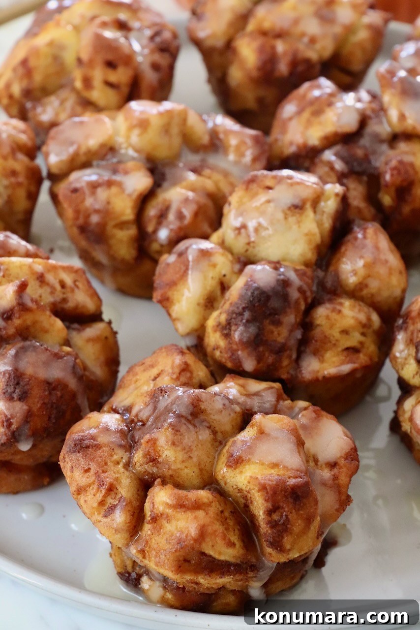 Maple-Glazed Pull-Apart Pumpkin Cinnamon Rolls 2 pull apart pumpkin cinnamon rolls on a plate drizzled with cream cheese icing