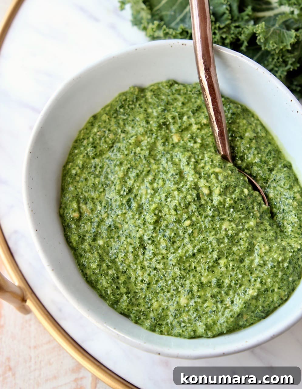Kale pesto in white bowl with copper spoon in the bowl