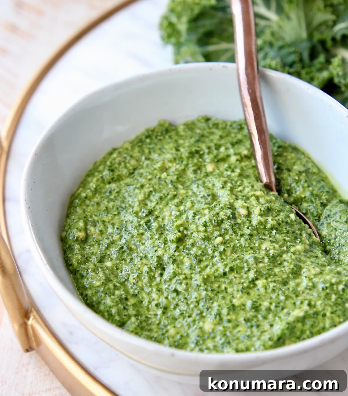 Kale pesto in white bowl with copper spoon